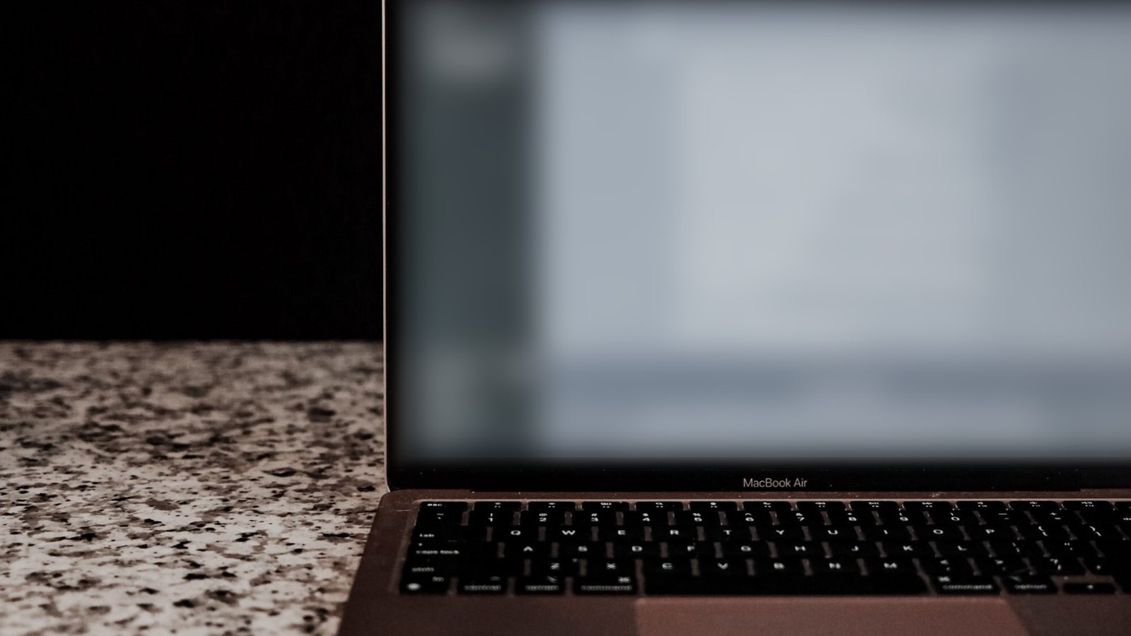 An open laptop on a granite worktop against a dark background.