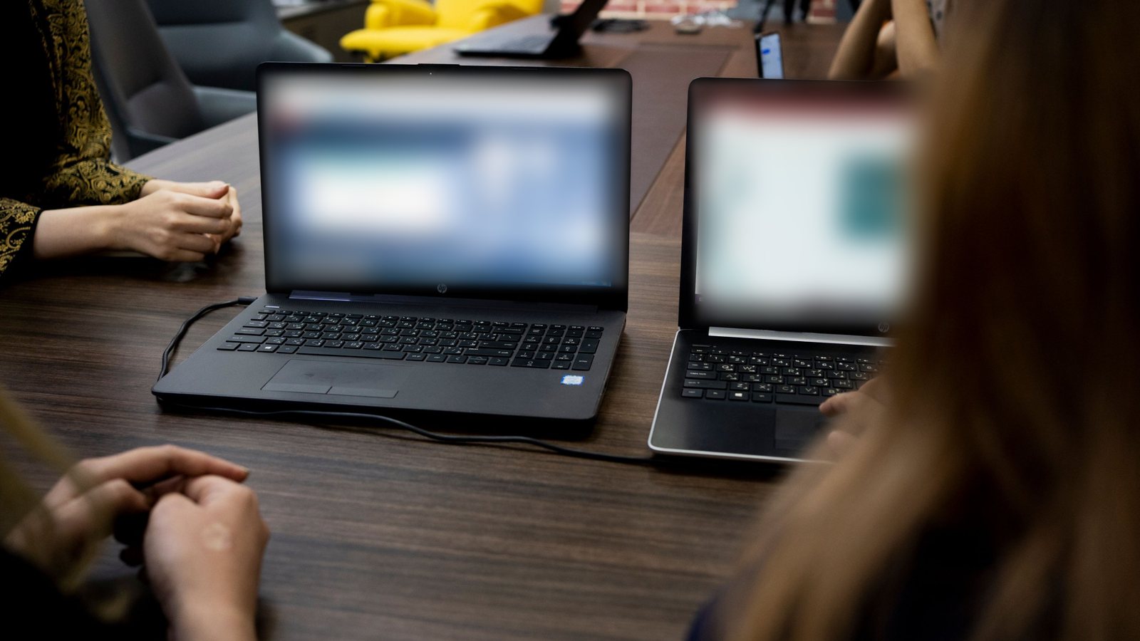 Two laptops on a meeting table with people sitting around it.